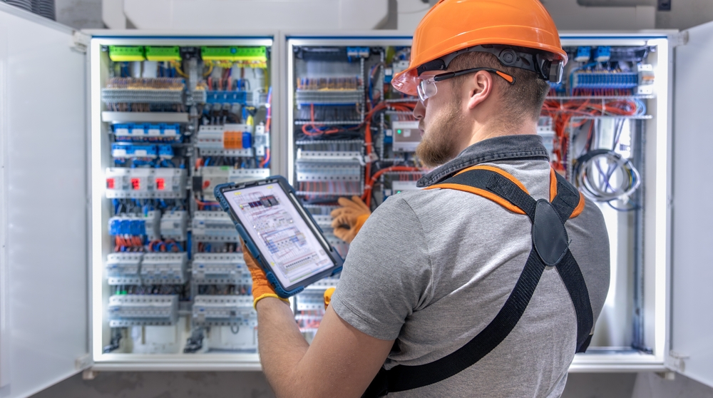 Image of an electrician using a tablet to inspect an electrical panel in a commercial property.